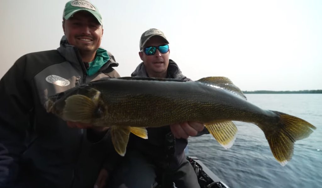 Two people in outdoor gear and hats smile while holding a large fish together on a boat, with water and a hazy sky behind them—an exciting moment captured with the help of their fishing guide.